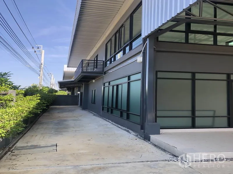 Factory for rent or sale in Bang Bo, Samut Prakan - Side driveway beside glazed office windows and balcony under deep roof eave.