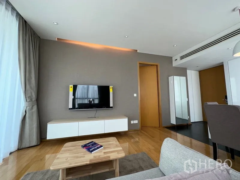 公寓 出租在Watthana, Bangkok - 采光充足的客厅，墙面挂电视、悬空电视柜、木地板与落地窗帘。