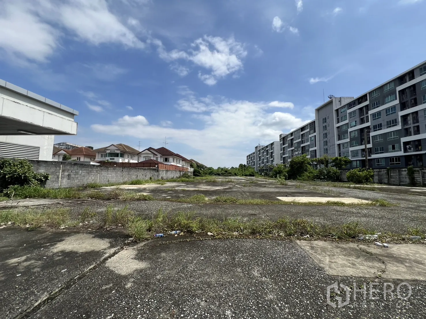 Land for sale in Bang Kapi, Bangkok - Front area of the plot with grass tufts on old concrete, condos lining the right side.