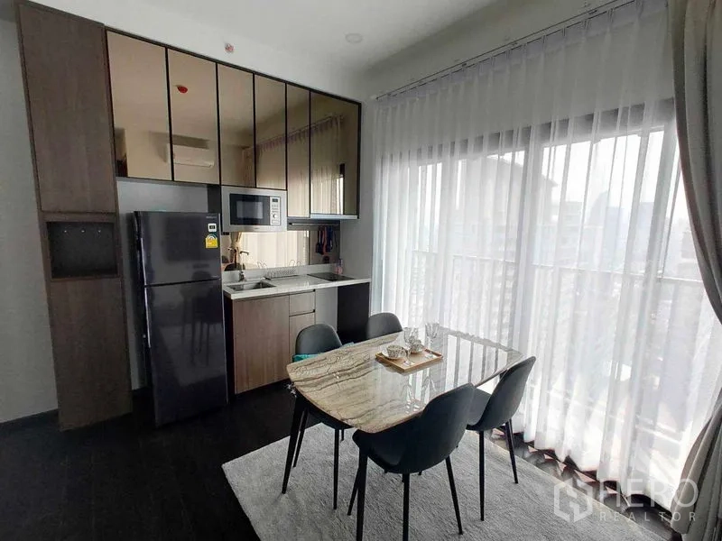 Condominium for rent in Watthana, Bangkok - Bright dining area with a marble table beside a compact kitchen and full-height windows.