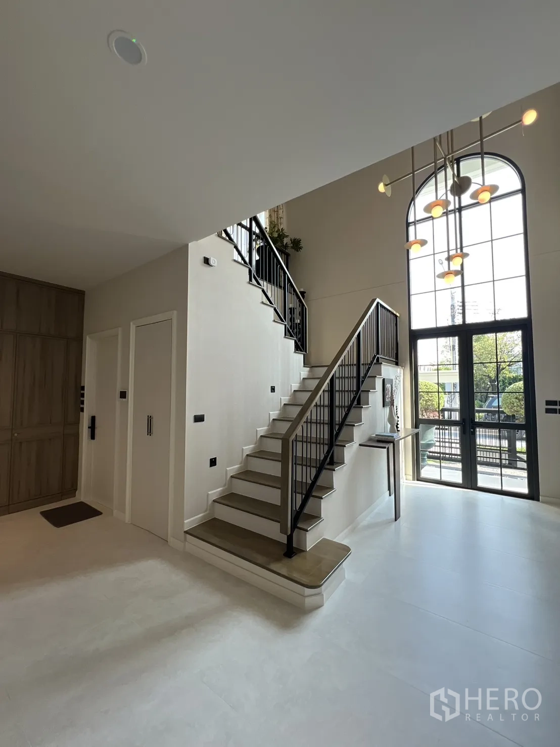 独栋房屋 for rent in Bang Phli, Samut Prakan - 挑高玄关，黑色栏杆楼梯与拱形落地窗，搭配吊灯。