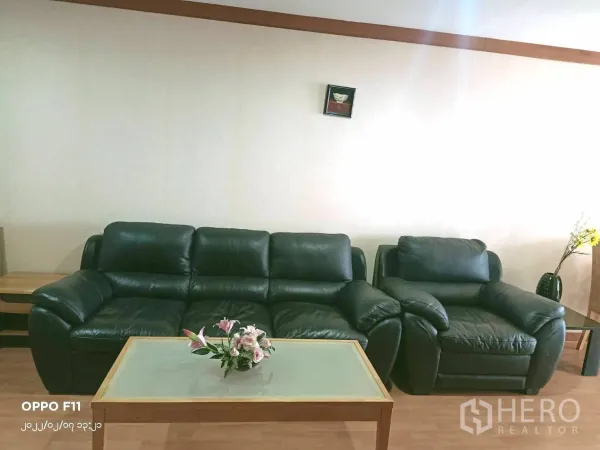 Condominium for rent in Khlong Toei, Bangkok - Cozy living room with black leather sofa set and glass coffee table against a neutral wall.