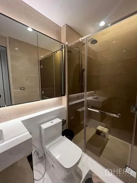 Condominium for sale - Compact bathroom with glass-enclosed shower, toilet, and wide mirrored cabinet.