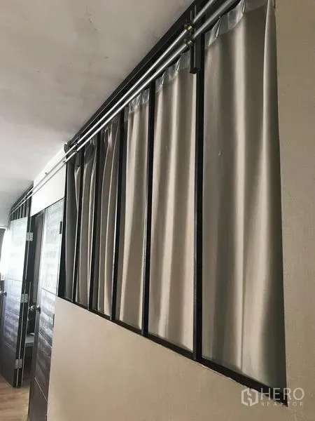 Condominium for rent in Phaya Thai, Bangkok - Hallway with metal frame and ceiling rails holding grey curtains next to wooden doors in the condominium.