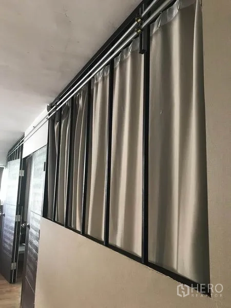 Condominium for rent in Phaya Thai, Bangkok - Hallway with metal frame and ceiling rails holding grey curtains next to wooden doors in the condominium.