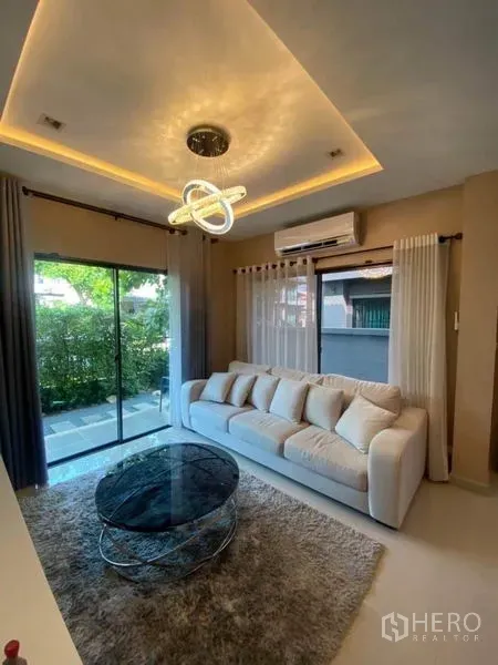 Detached House for rent or sale in Saphan Sung, Bangkok - Cozy living room with sofa, glass coffee table and sliding doors to the garden.
