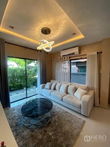Detached House for rent or sale in Saphan Sung, Bangkok - Cozy living room with sofa, glass coffee table and sliding doors to the garden.