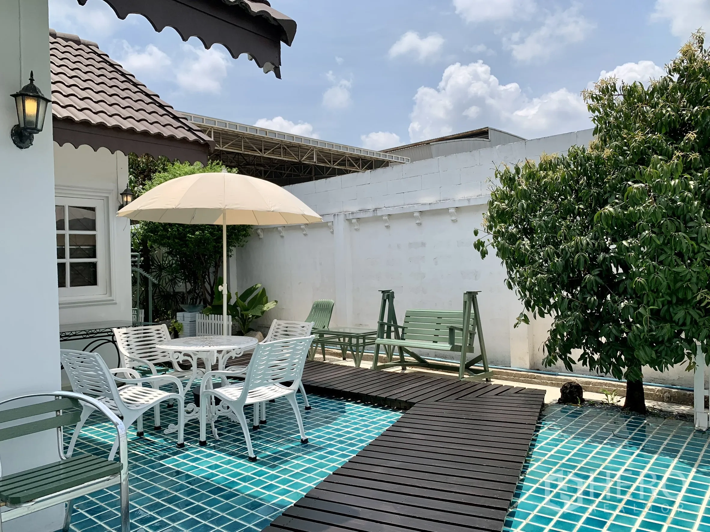 独栋房屋 for rent in Saphan Sung, Bangkok - 露台休闲区配遮阳伞与木栈道，秋千座椅与树木沿白墙分布。