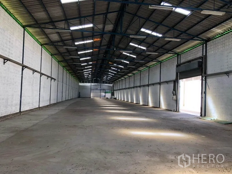 Factory for rent in Nonthaburi - Warehouse interior showing roller-shutter loading door, bright skylights and wide column-free space.