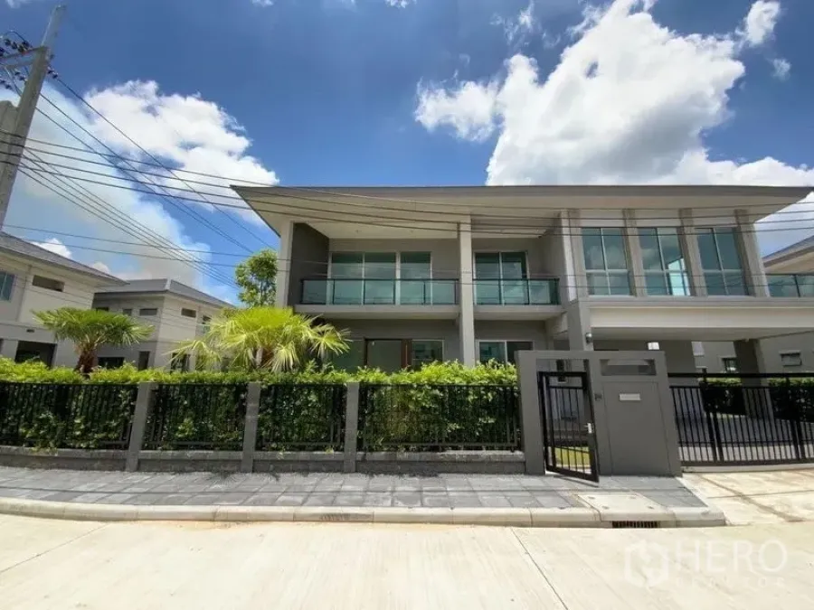Townhouse for rent in Prawet, Bangkok - Modern two-storey townhouse exterior with glass balconies, front gate and landscaped garden under blue sky.