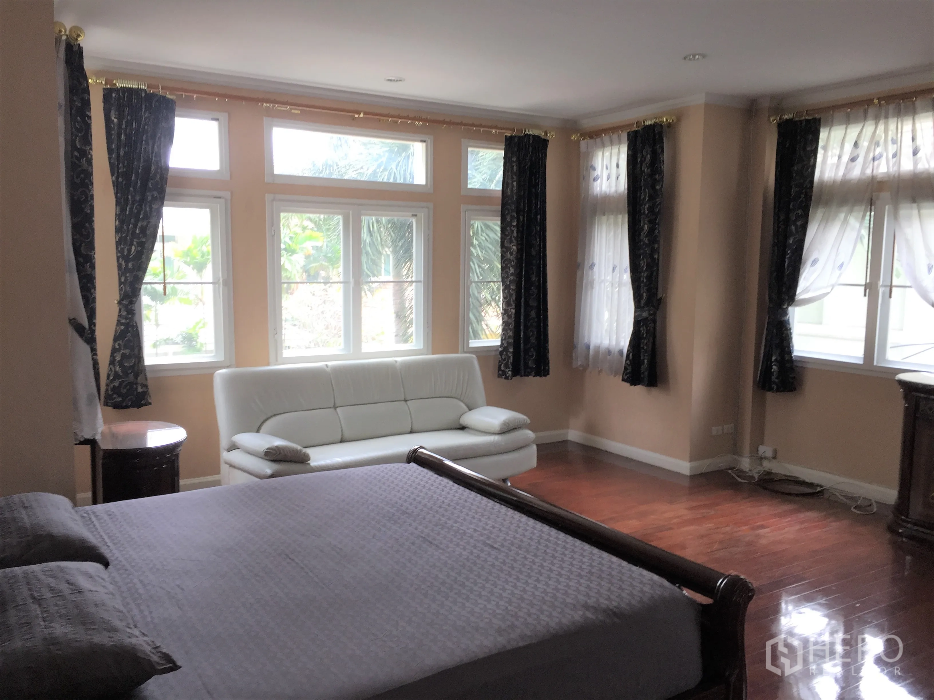 Detached House for rent or sale in Lat Phrao, Bangkok - Large master bedroom with bay windows, hardwood floors and a white sofa.