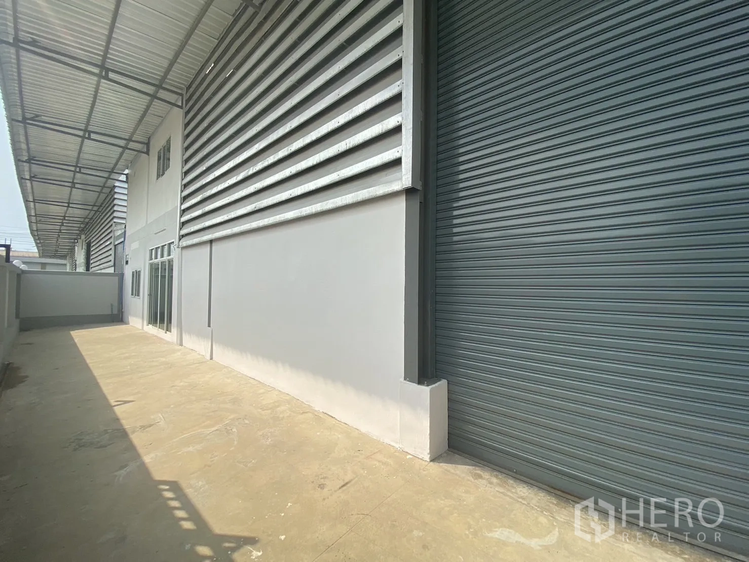 โรงงาน for rent or sale in Mueang Samut Sakhon, Samut Sakhon - มุมมองด้านข้างของโรงงานพร้อมประตูม้วนใหญ่และลานคอนกรีตยาว