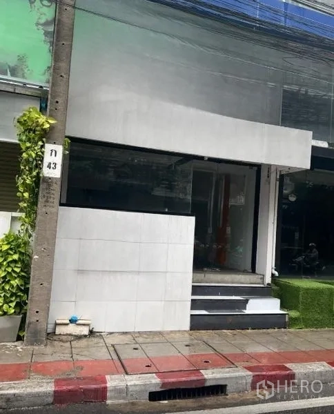 Retail Space for rent in Watthana, Bangkok - Street-level retail shopfront with white facade, large glass window, steps and sidewalk in an urban Bangkok setting.