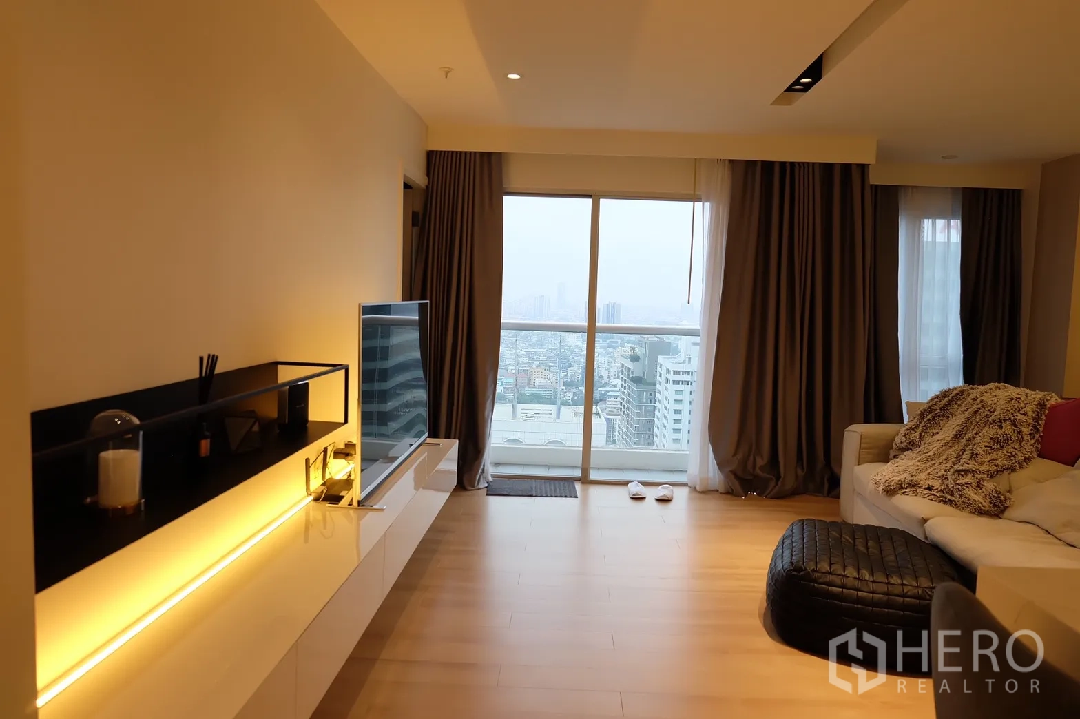 Condominium for rent in Bang Rak, Bangkok - Bright living room with TV wall, balcony and skyline view over Bang Rak.