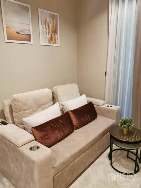 公寓 出租或出售在Ratchathewi, Bangkok - 紧凑休闲角，双人沙发、边几与墙面装饰画，氛围舒适。
