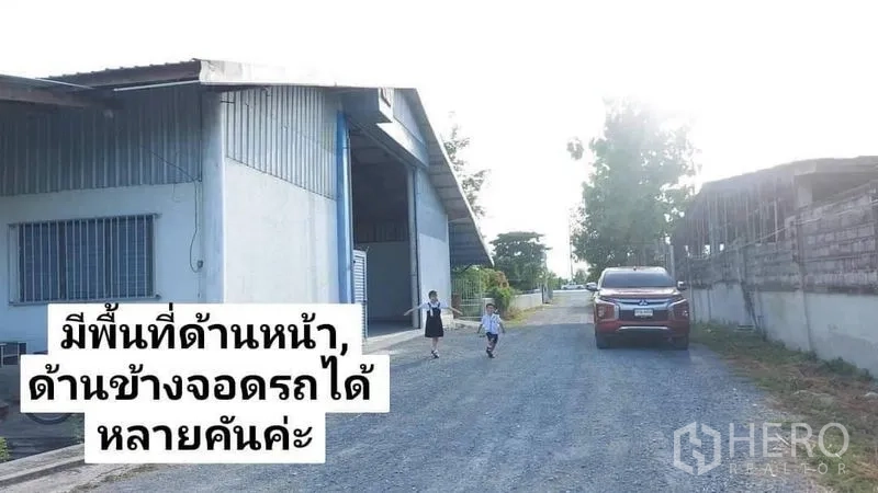 Warehouse for rent in Nakhon Pathom - Warehouse exterior along a gravel road with generous setback and multiple parking spaces.