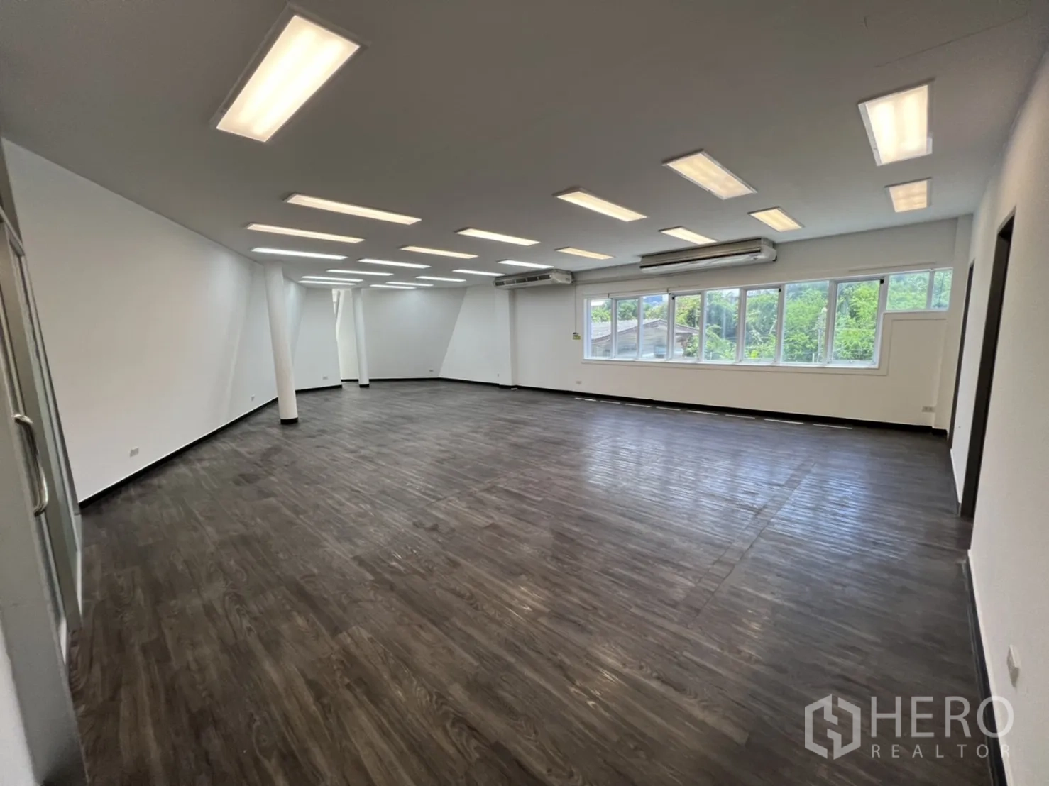 Retail Space for rent in Sathon, Bangkok - Open office hall with rows of ceiling lights and green views through windows.