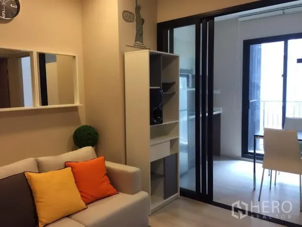 公寓 出售在Huai Khwang, Bangkok - 舒适客厅配沙发与置物架，通过推拉玻璃门连接小厨房与阳台。