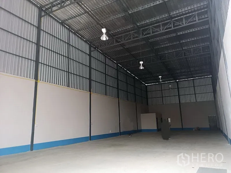 Warehouse for rent in Prawet, Bangkok - Long clear-span warehouse bay with corrugated metal walls, bright ceiling fixtures and open storage space.