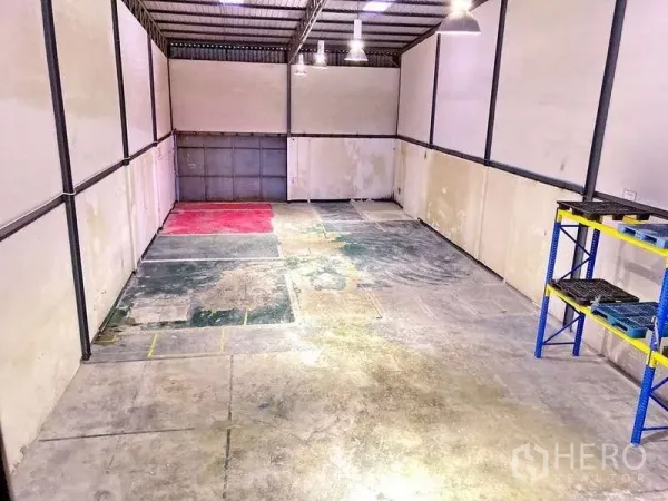 Factory for rent in Samut Prakan - Warehouse interior with high ceiling, pendant lights and concrete floor, showing marked work zones.