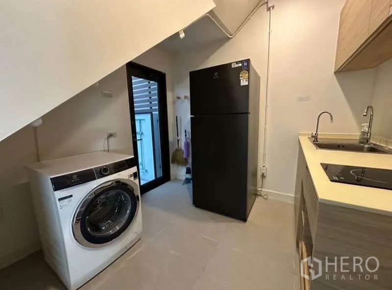 Townhouse for rent in Lat Phrao, Bangkok - Utility kitchen with sink, induction hob, refrigerator and washing machine.