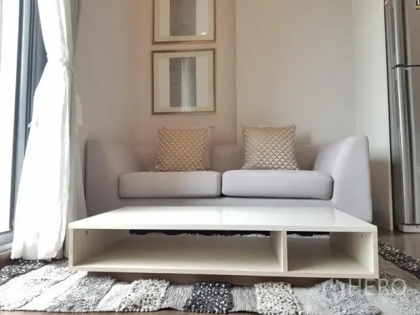 Condominium for rent in Ratchathewi, Bangkok - Cozy gray sofa with patterned cushions and a low white coffee table beneath framed wall art.