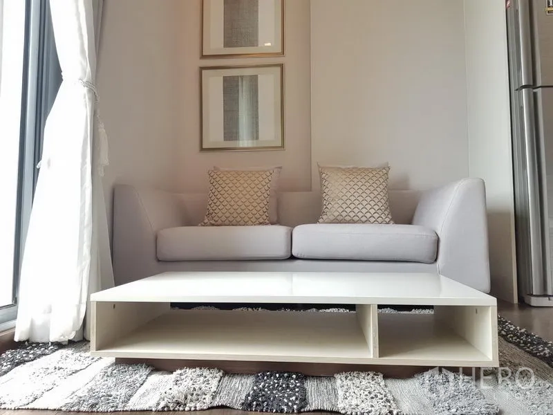 Condominium for rent in Ratchathewi, Bangkok - Cozy gray sofa with patterned cushions and a low white coffee table beneath framed wall art.