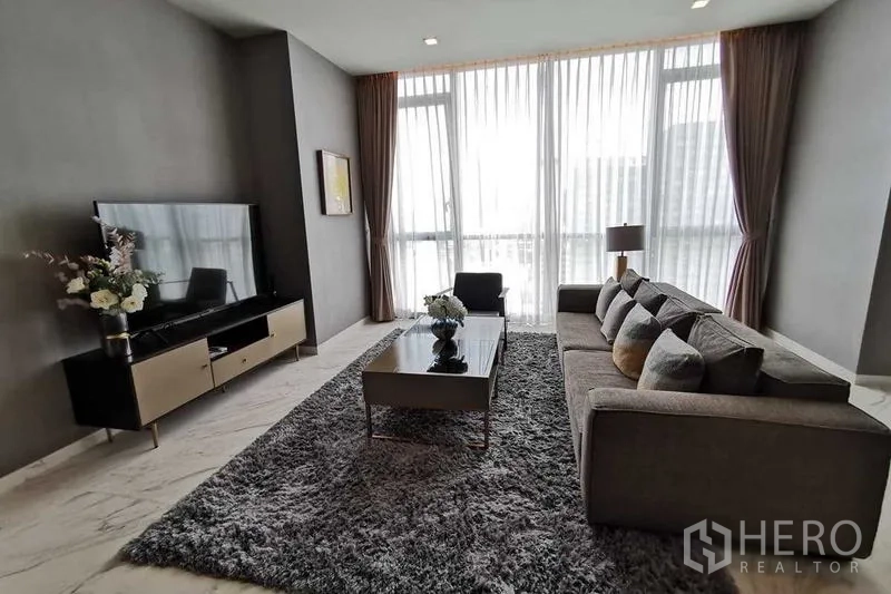 Condominium for rent or sale in Watthana, Bangkok - Cozy lounge with TV console, floral decor and tall curtains letting in light.