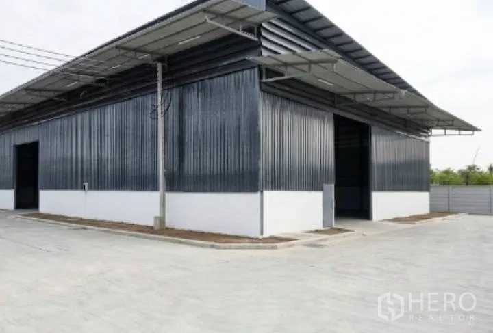 Warehouse for rent in Mueang Samut Sakhon, Samut Sakhon - Corner view of a metal-clad warehouse with roof canopies and driveway access.