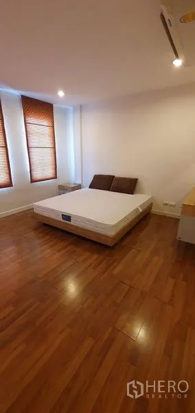 Townhouse for sale in Bang Kapi, Bangkok - Bedroom with wood flooring, recessed lights and three narrow windows with blinds.