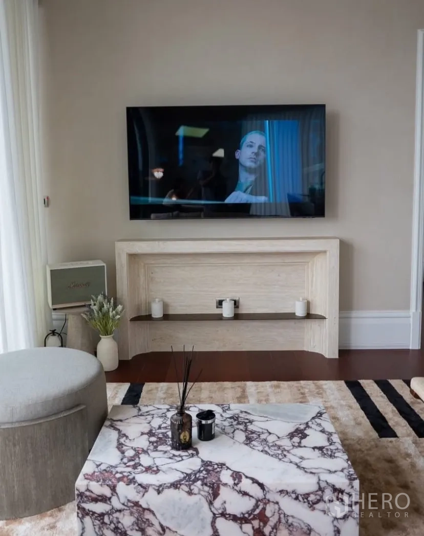 Condominium for rent or sale in Watthana, Bangkok - Living area with wall-mounted TV, marble coffee table and soft rug.