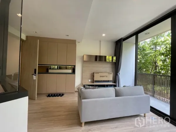 Condominium for sale in Watthana, Bangkok - Open-plan lounge with built-in storage cabinets and a balcony beyond the glass.
