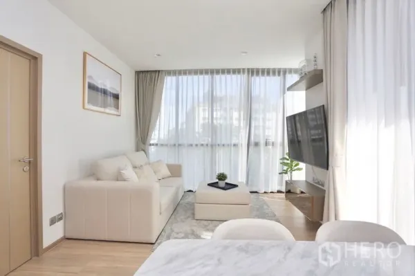 Condominium for rent or sale in Watthana, Bangkok - Open-plan living area with marble-top dining, sofa set, large windows and a built-in TV shelf.