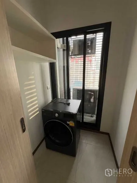 Condominium for rent in Ratchathewi, Bangkok - Laundry nook with front-load washing machine and vented sliding window.