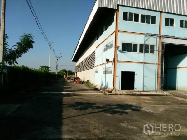 Factory for sale in Lat Lum Kaeo, Pathum Thani - Side service driveway along the warehouse for truck access, with utilities and greenery.