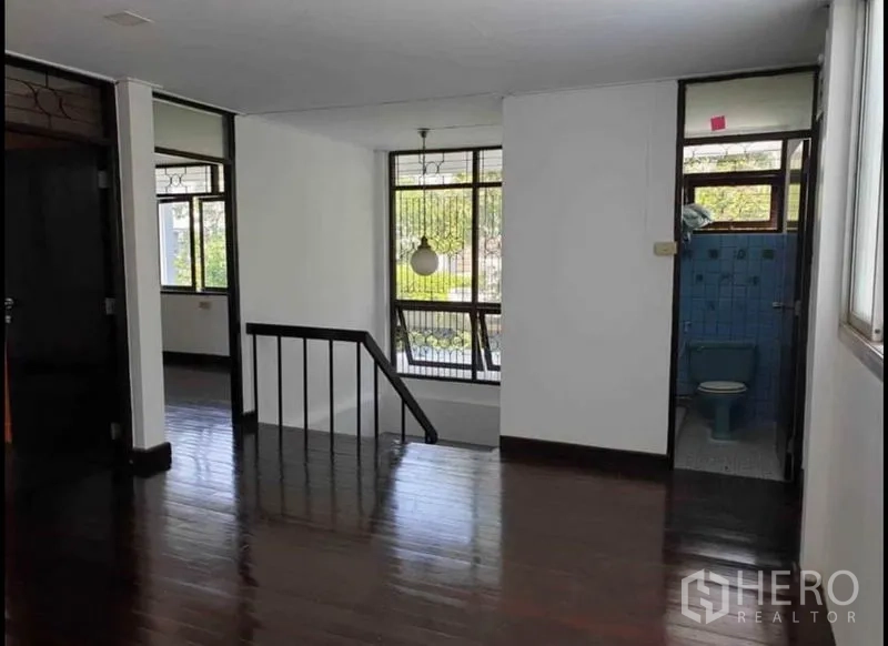 独立式住宅 出租在Lat Phrao, Bangkok - 二层楼梯平台，木地板、扶手与通向蓝色瓷砖卫生间的门。