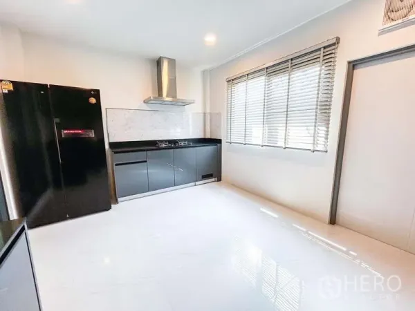 Detached House for rent in Bang Phli, Samut Prakan - Bright kitchen with black cabinetry, marble backsplash, range hood and large black fridge beside a window.