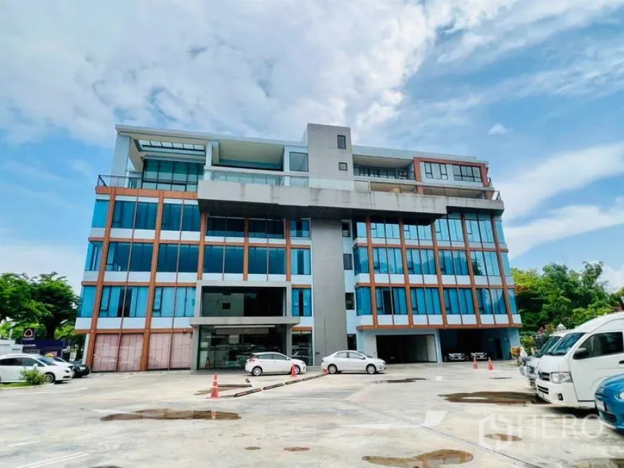 办公空间 出租在Khlong San, Bangkok - 中高层玻璃幕墙办公楼，前方设有停车区。