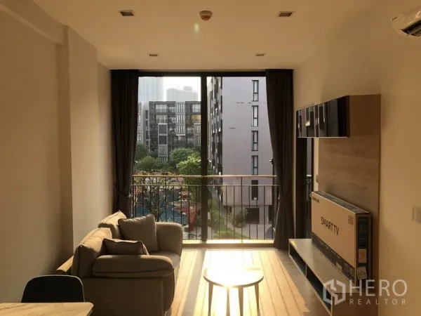 Condominium for rent in Watthana, Bangkok - Living area with floor-to-ceiling window and balcony overlooking a landscaped courtyard and pool.