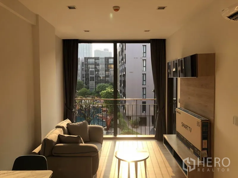 Condominium for rent in Watthana, Bangkok - Living area with floor-to-ceiling window and balcony overlooking a landscaped courtyard and pool.