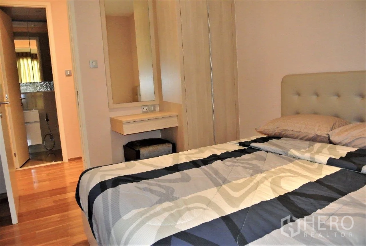 Condominium for rent in Watthana, Bangkok - Cozy bedroom with built-in wardrobe, vanity and ensuite access, featuring warm wood floors and soft lighting.