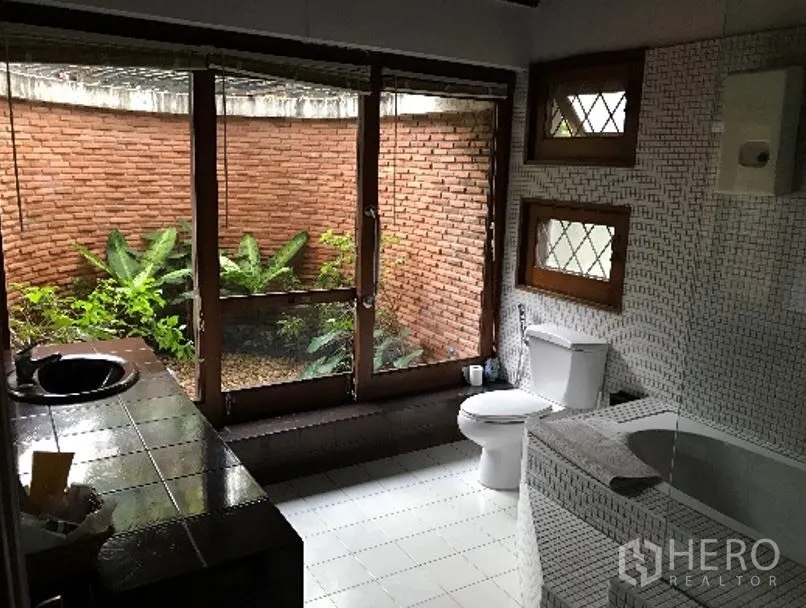 独立式住宅 出租在Khlong Toei, Bangkok - 浴室带浴缸，落地玻璃门通向小花园与红砖围墙。