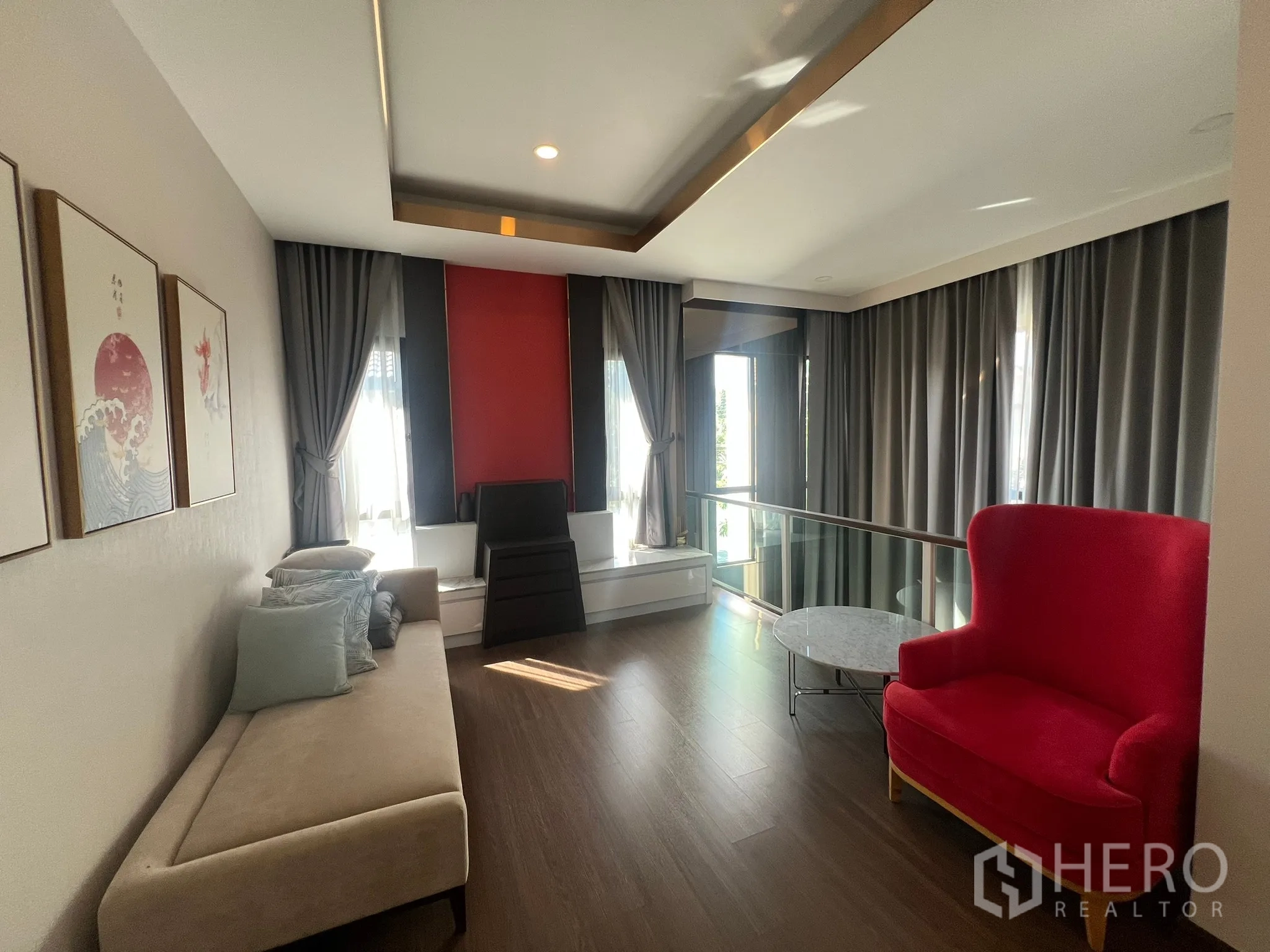 Detached House for rent or sale in Prawet, Bangkok - Upper family living area with sofa, red accent wall and glass balustrade.