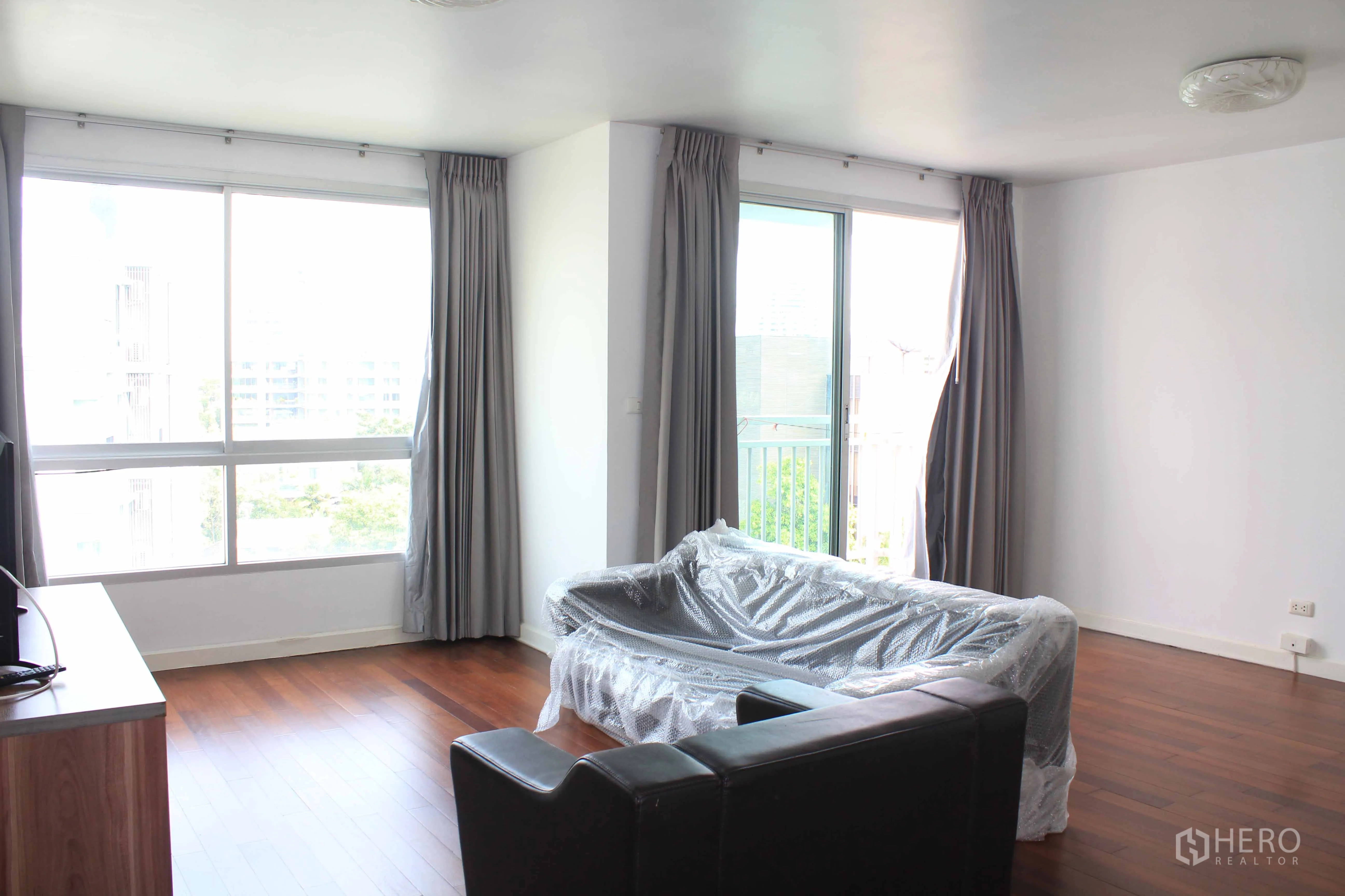 คอนโด ให้เช่าในWatthana, Bangkok - ห้องนั่งเล่นมุมอาคาร หน้าต่างสูงเต็มบาน ประตูกระจกสไลด์ออกระเบียง และโซฟาคลุมพลาสติก