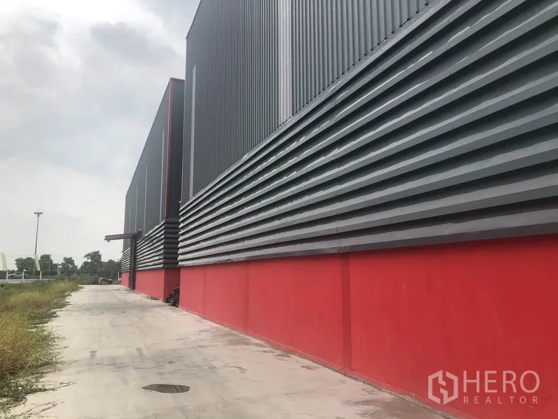 货栈 出租在Khlong Luang, Pathum Thani - 仓库长侧立面，通风金属板、服务步道与周边绿地。