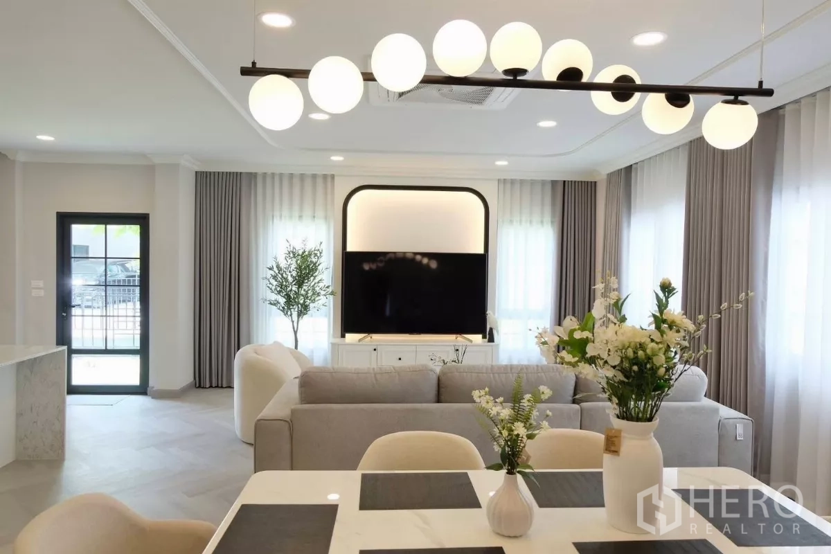独立式住宅 出售在Bang Phli, Samut Prakan - 餐厅视角，可见球形吊灯、鲜花摆设、落地窗与客厅电视墙