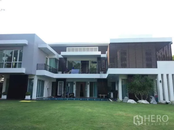 บ้าน ขายในMin Buri, Bangkok - มุมมองด้านหลังบ้านพร้อมสนามหญ้ากว้างและผนังกระจกสูงต่อเนื่องสู่ลานพักผ่อน