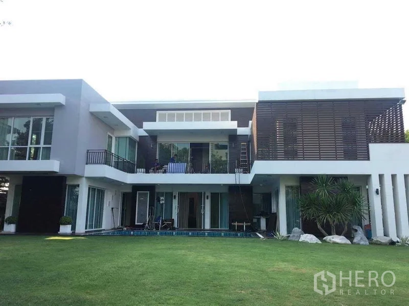 บ้าน ขายในMin Buri, Bangkok - มุมมองด้านหลังบ้านพร้อมสนามหญ้ากว้างและผนังกระจกสูงต่อเนื่องสู่ลานพักผ่อน