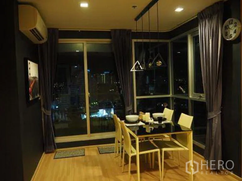 公寓 出租在Sathon, Bangkok - 转角用餐区，玻璃餐桌与吊灯，临窗可观城市灯光。