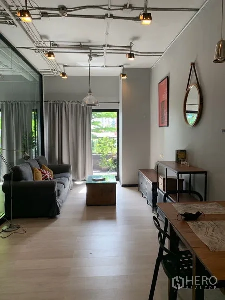 คอนโด ขายในWatthana, Bangkok - ห้องนั่งเล่นสว่างด้วยโซฟาสีเทา ไฟห้อย พื้นไม้โทนอ่อน และประตูกระจกเปิดสู่ระเบียงที่ร่มรื่น